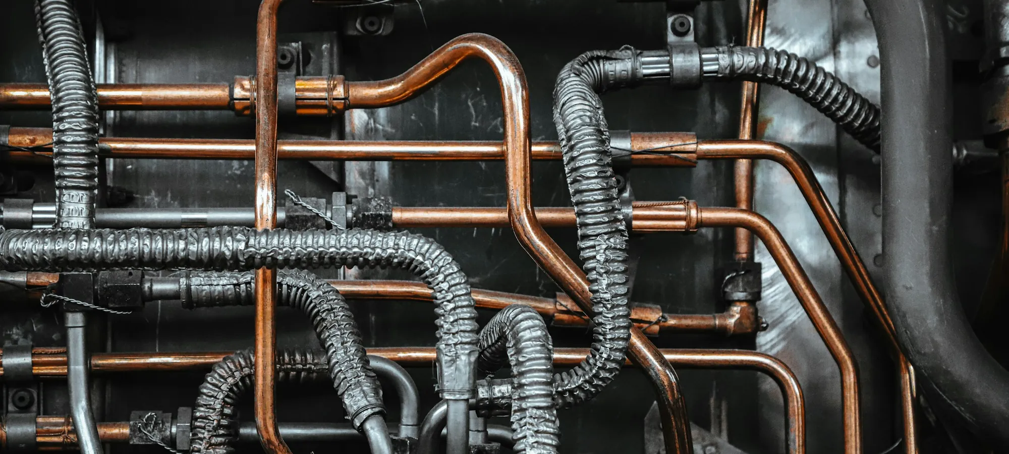 Close-up of copper heat lines and braided hoses running across a dark equipment panel